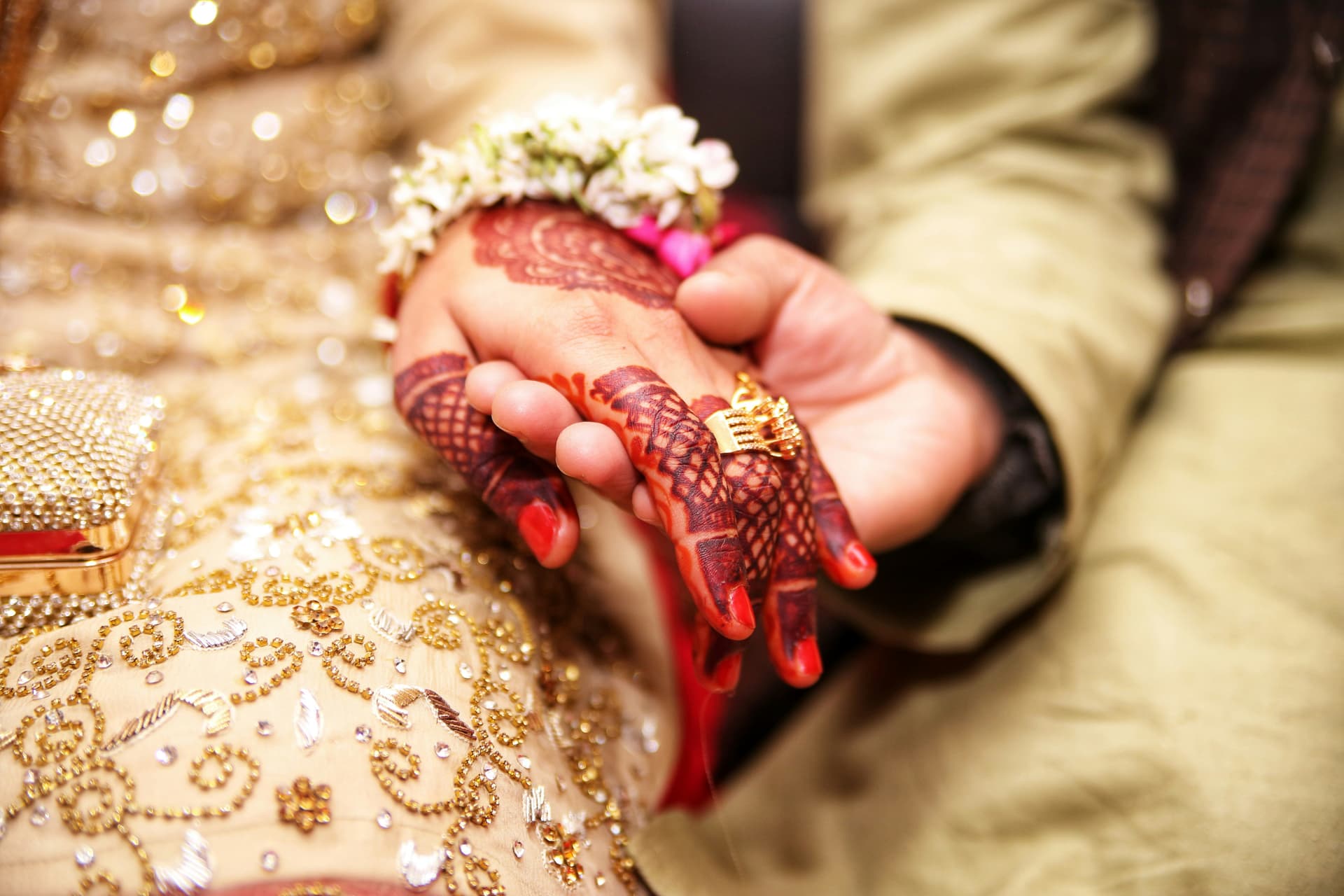 Bride and groom holding hands — intricate mehndi and gold ring